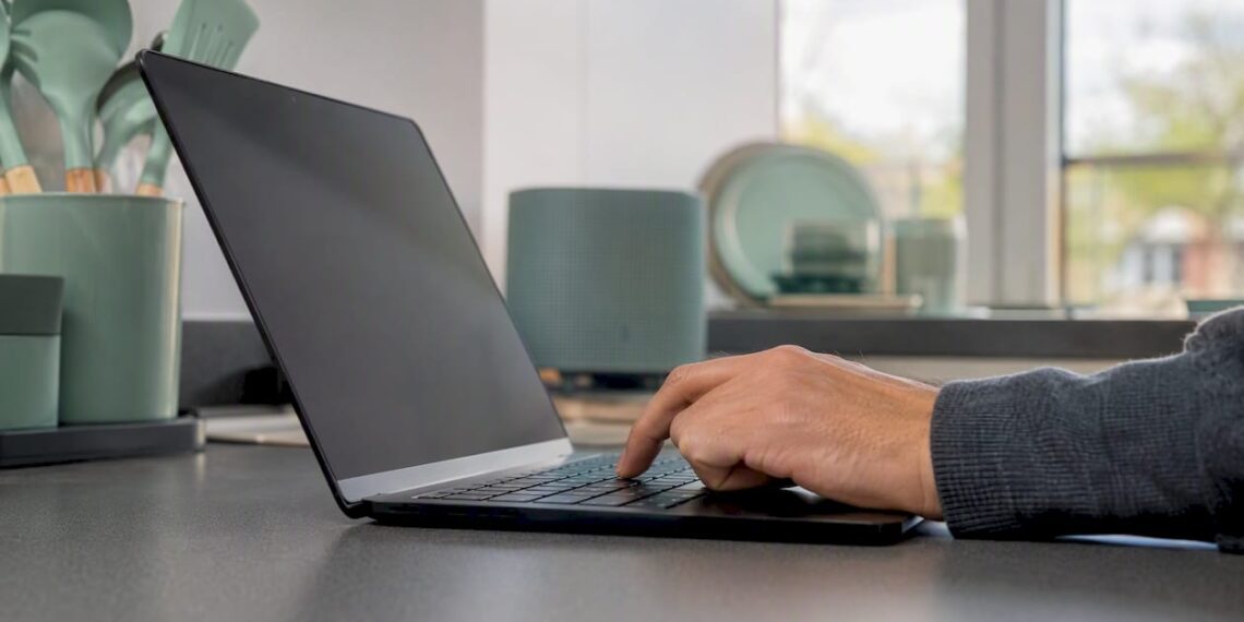 Eine Hand tippt auf einer Tastatur neben einem Laptop im Büro.