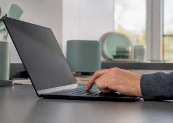 Eine Hand tippt auf einer Tastatur neben einem Laptop im Büro.