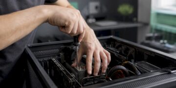 Jemand arbeitet mit den Händen am geöffneten PC-Gehäuse und repariert die Hardware.