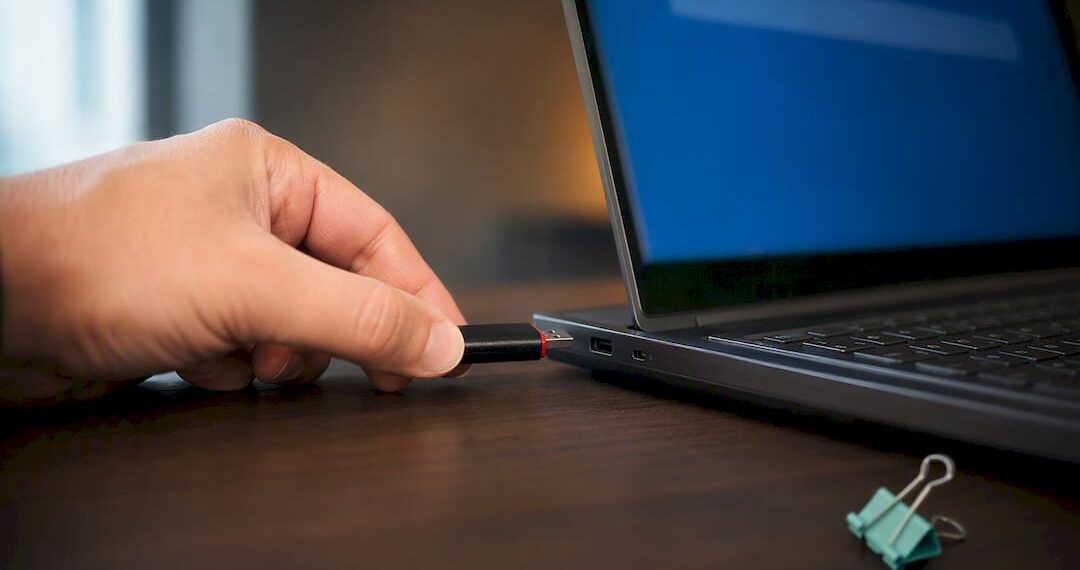 Hand hält USB-Stick neben gesperrtem Laptop