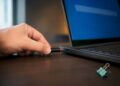 Hand hält USB-Stick neben gesperrtem Laptop